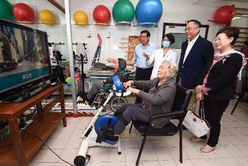The Secretary for Innovation and Technology, Mr Nicholas W Yang (second right), watches an elderly lady undergoing rehabilitation training on an exercise bicycle with a physically activated screen at the Buddhist Li Ka Shing Care and Attention Home for the Elderly today (May 27). Also present is the Chairman of the Wan Chai District Council, Mr Stephen Ng (first left).